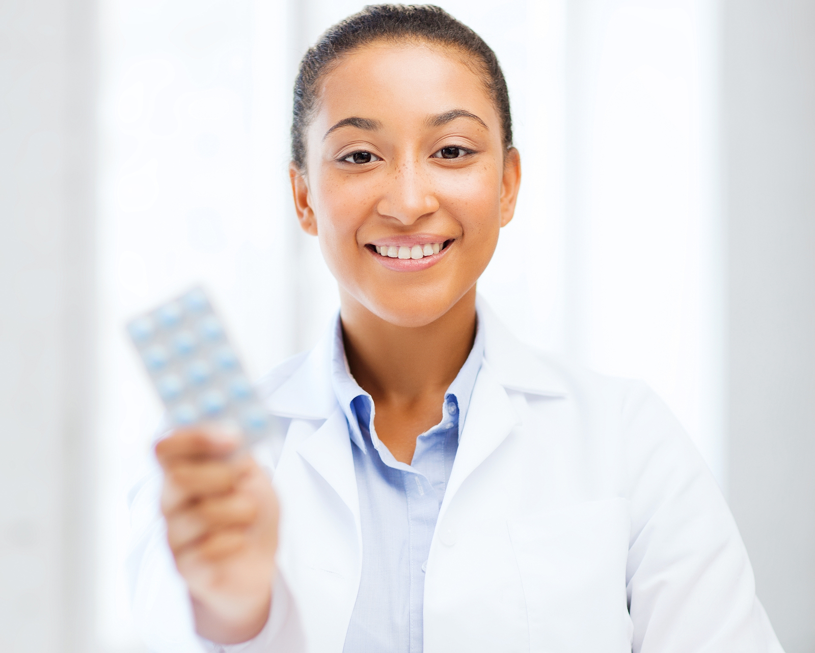 Woman in white coat holds up pack of birth control pills