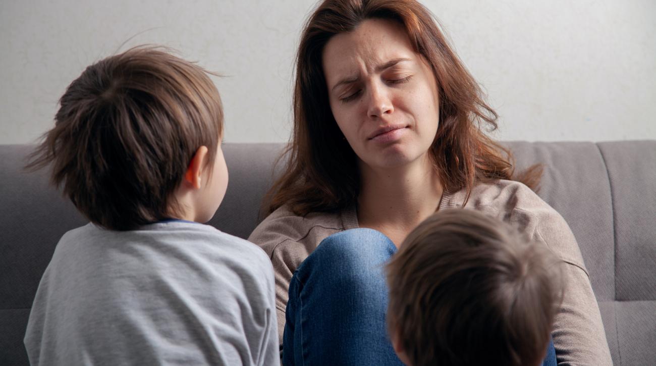 Woman with pained expression sitting on couch with two small children