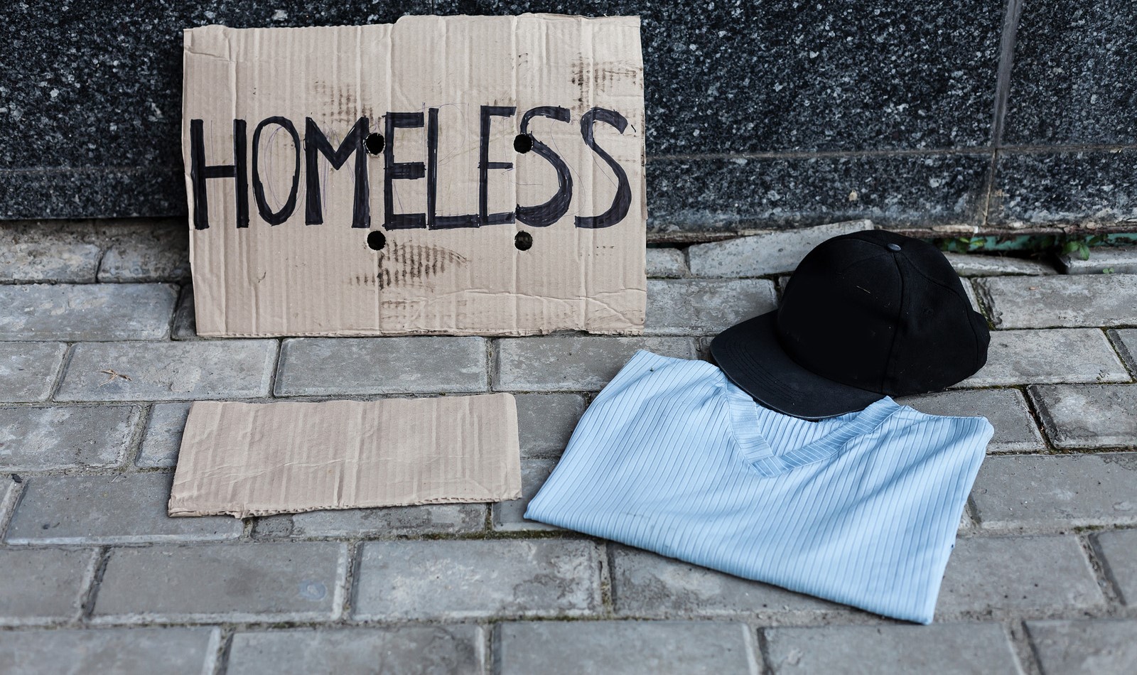 Cardboard "homeless" sign next to cap and folded shirt