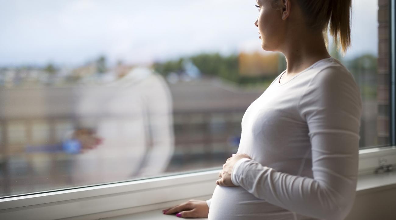 Pensive pregnant woman standing by window