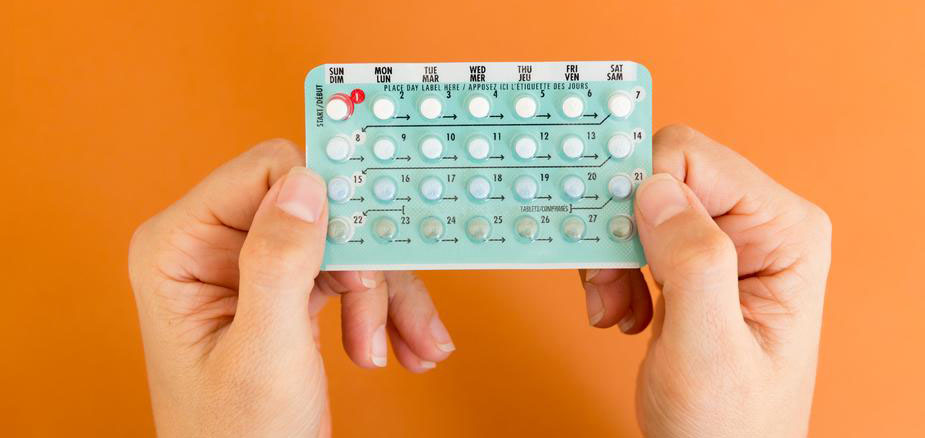 Two hands hold pack of birth control pills against orange background