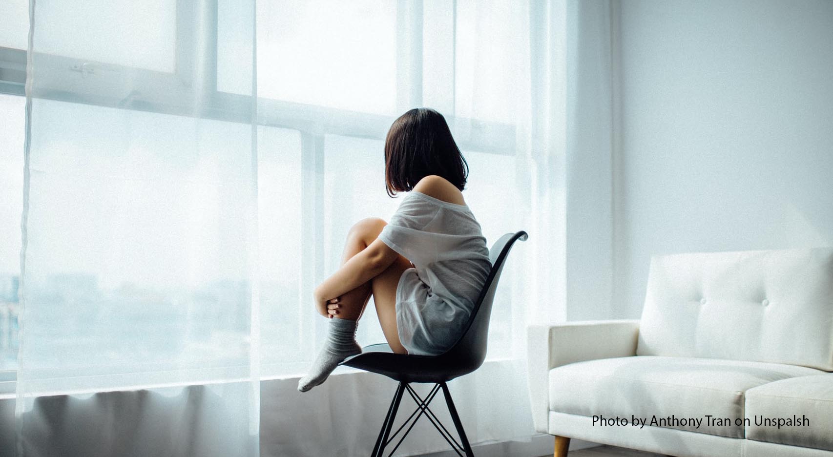 Back view of woman sitting curled on a chair by a window