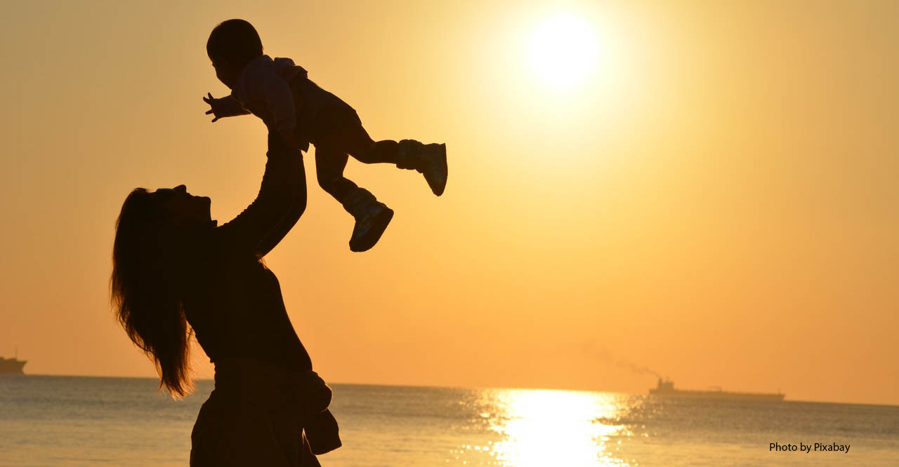 Silhouette of woman holding a child in front of a sunset at the beach