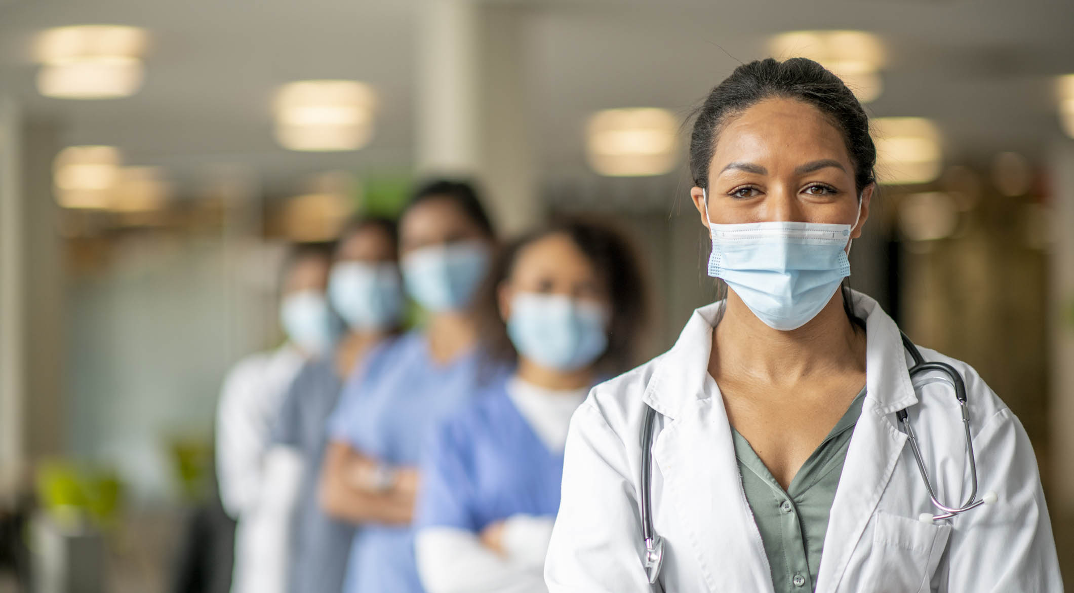 Woman in surgical mask and doctor's coat standing in front of others in surgical masks