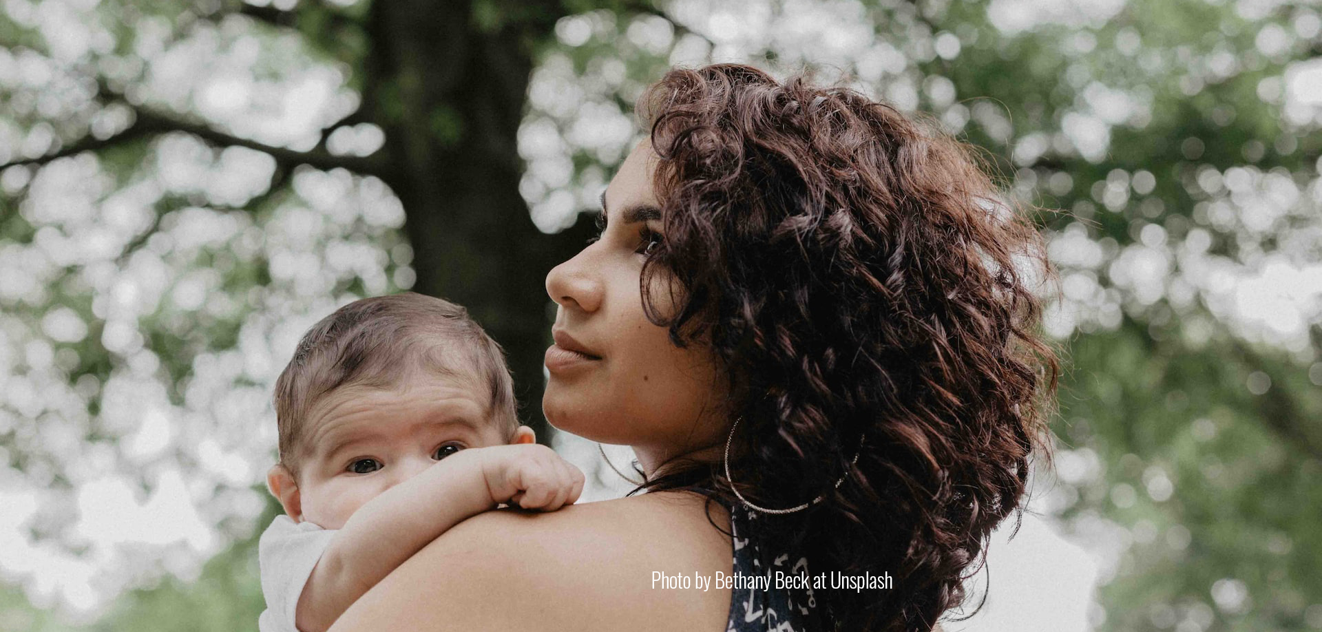 Woman with curly hair holding baby and looking over her shoulder