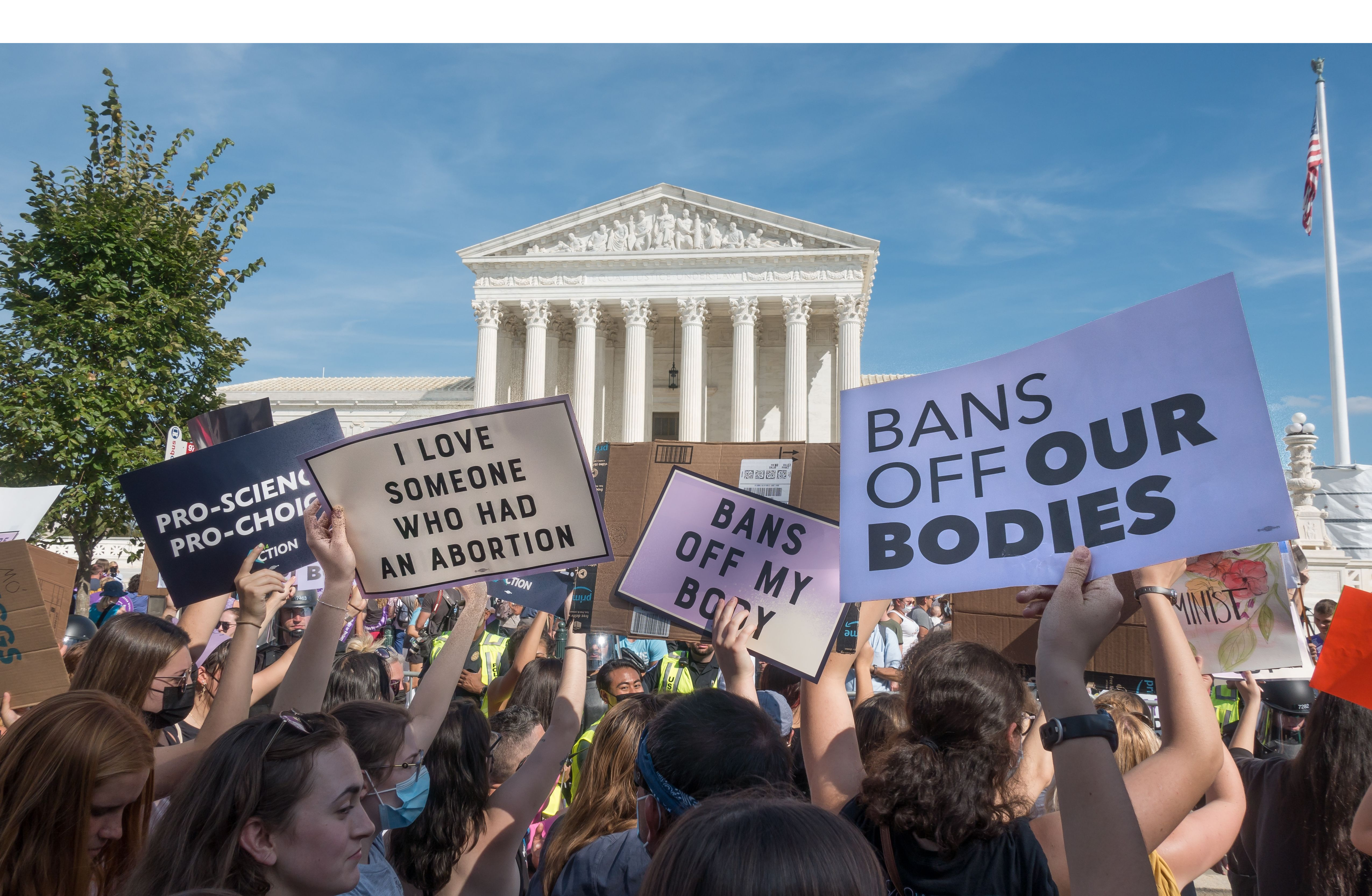 With the Supreme Court behind them, protestors hold signs reading "Bans off our bodies" and "I love someone who had an abortion"