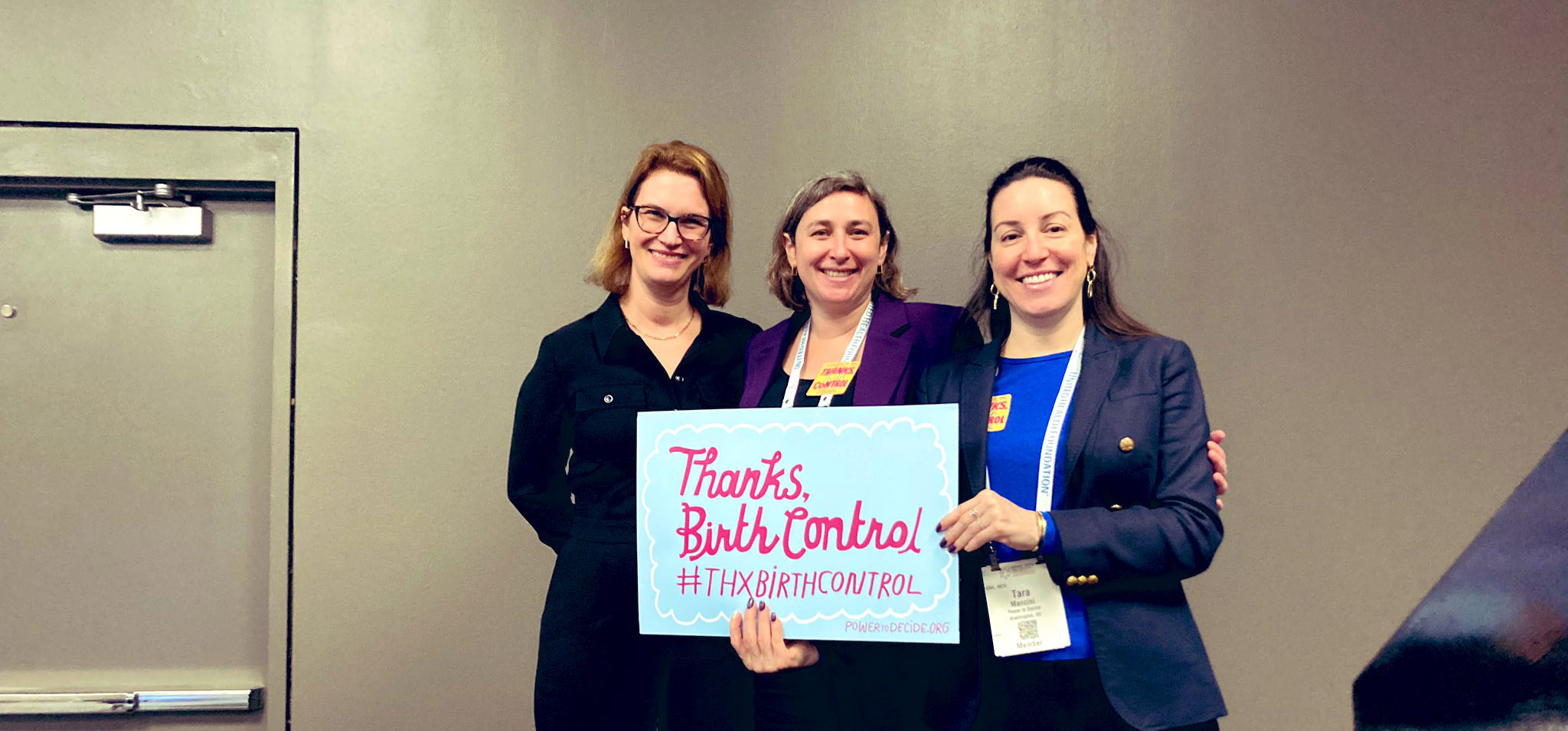 Three smiling white women in suits hold a sign that reads "Thanks Birth Control"