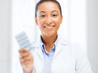 Woman in white coat holds up pack of birth control pills