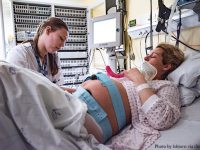 White-presenting pregnant woman in a hospital bed with a fetal monitor strapped across her belly speaks with another white-presenting woman in a white coat
