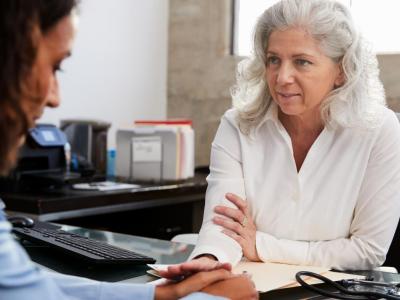 Gray-haired woman at desk pats hand of woman sitting across from her