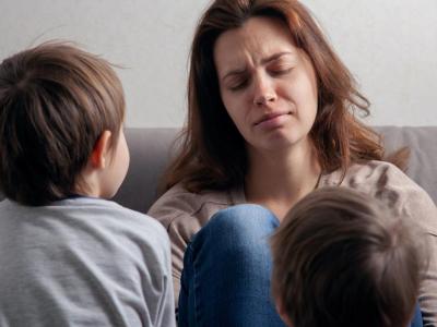 Woman with pained expression sitting on couch with two small children