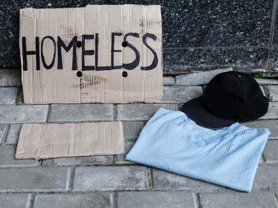 Cardboard "homeless" sign next to cap and folded shirt
