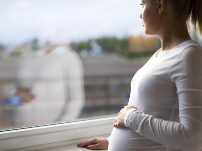 Pensive pregnant woman standing by window