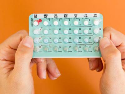 Two hands hold pack of birth control pills against orange background