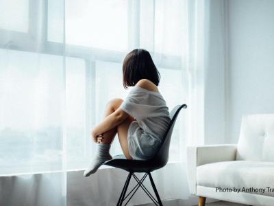 Back view of woman sitting curled on a chair by a window