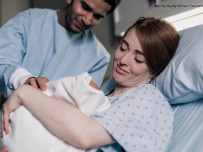 Woman in hospital bed smiles down at baby she's holding