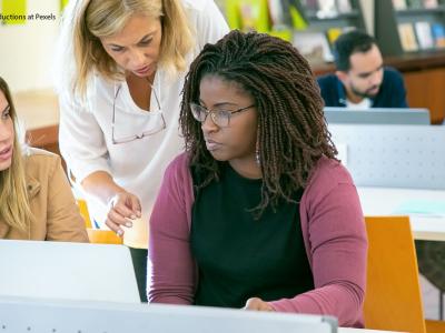 Older woman talking to young women sitting in front of computer