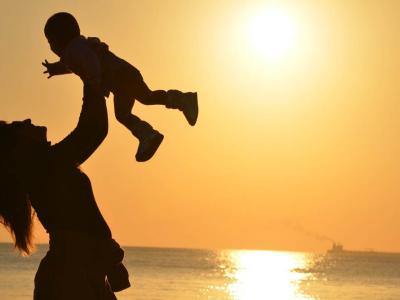 Silhouette of woman holding a child in front of a sunset at the beach