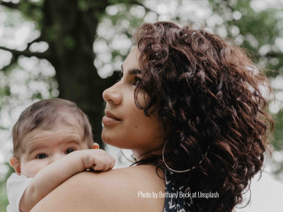 Woman with curly hair holding baby and looking over her shoulder