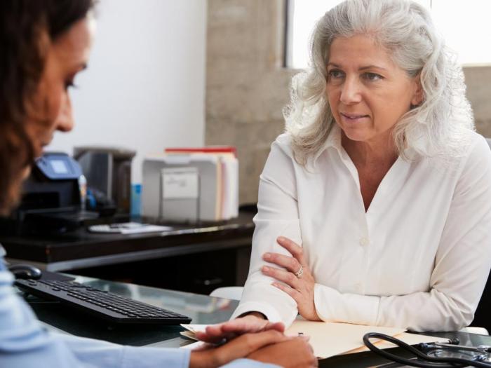 Gray-haired woman at desk pats hand of woman sitting across from her