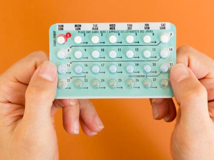 Two hands hold pack of birth control pills against orange background