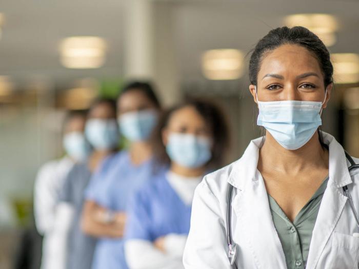 Woman in surgical mask and doctor's coat standing in front of others in surgical masks