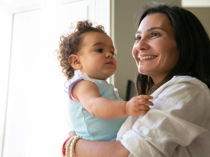 Smiling woman with dark hair and white skin holding a curly-haired infant