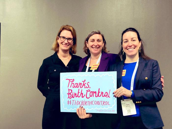 Three smiling white women in suits hold a sign that reads "Thanks Birth Control"