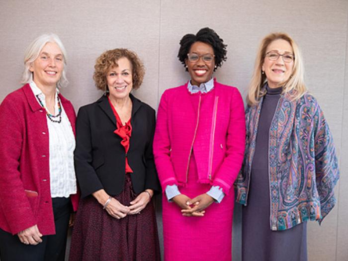 Four smiling women stand against a grey backdrop